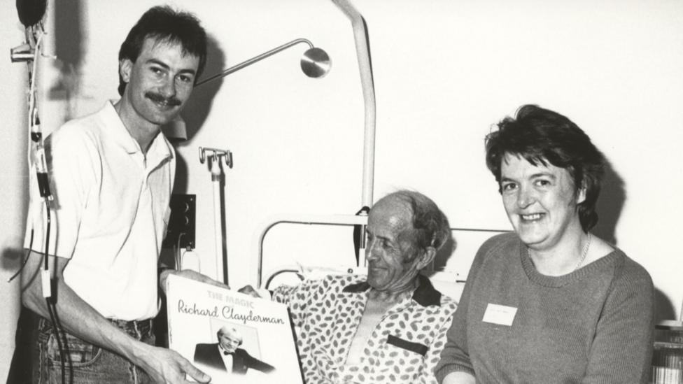 Dau berson yn ymweld a chlaf yn yr ysbyty