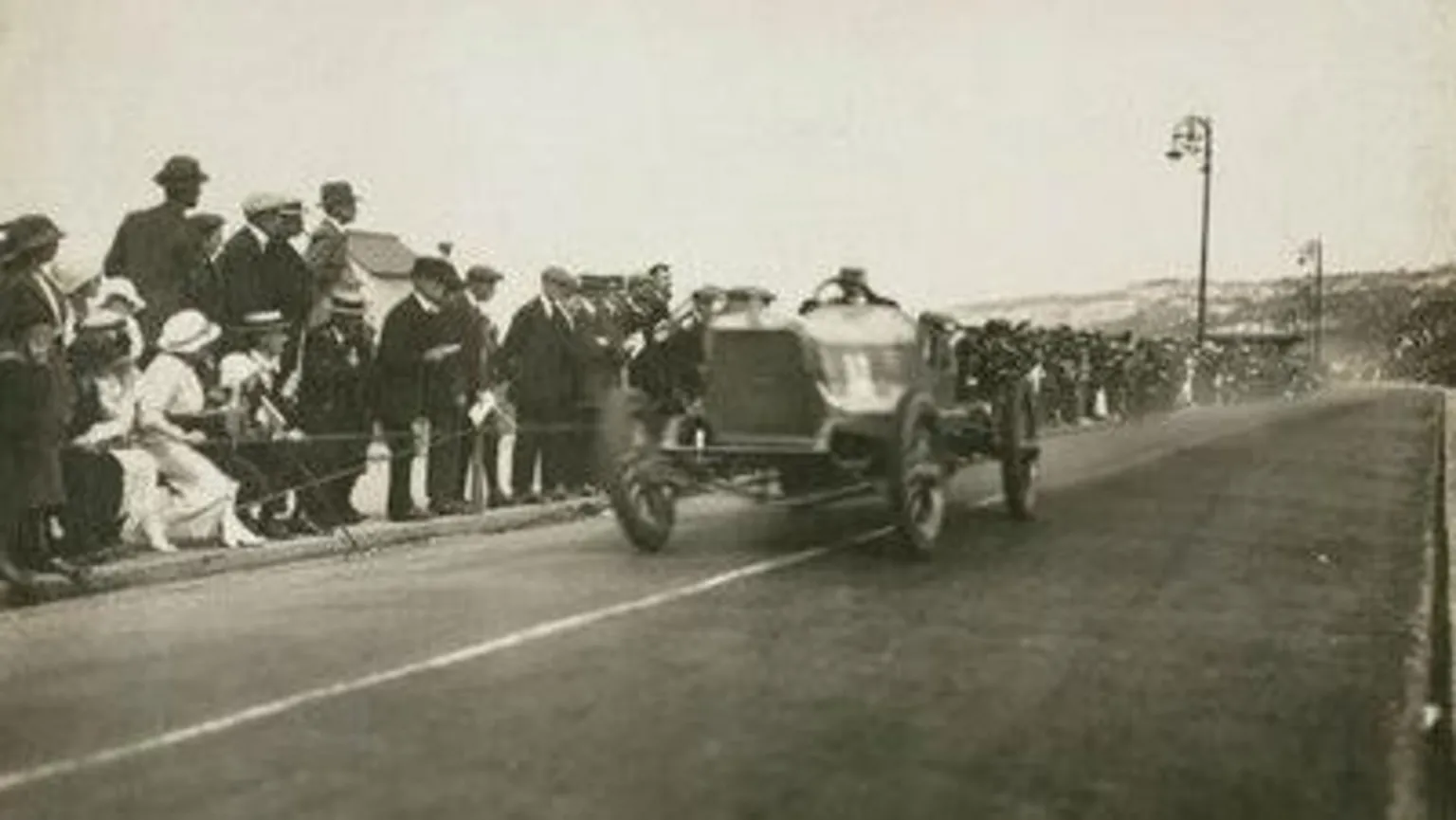 Autocar Magazine Crowds, as far as the eye can see, press against a rope barrier as a Talbot racing car speeds by. A lady dressed entirely in white, from stockings to hat, leans over to get an even closer view