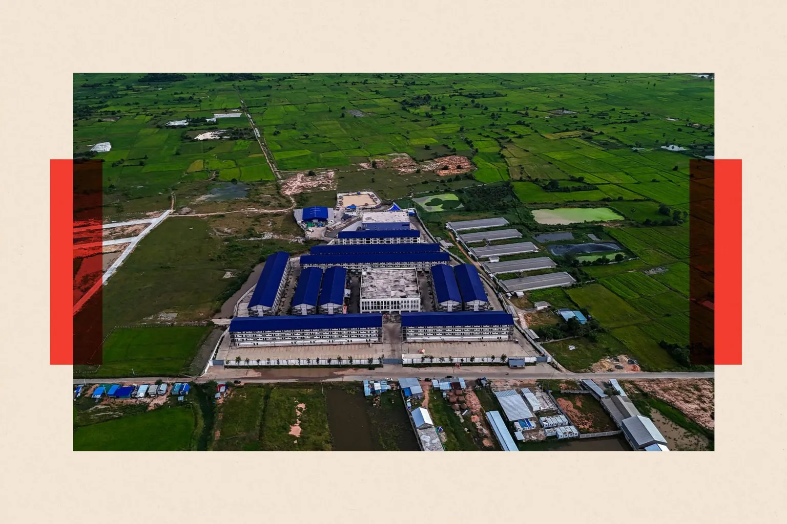  An aerial view showing a large compound made up of multiple buildings with blue roofs in the middle of an area with green fields