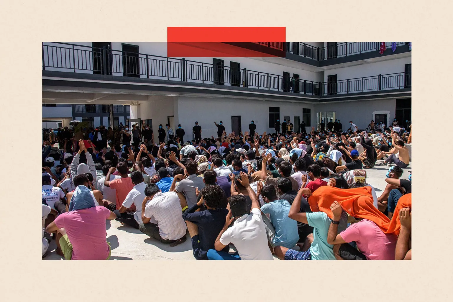  Hundreds of people sit cross legged in rows on a floor in an outdoors atrium