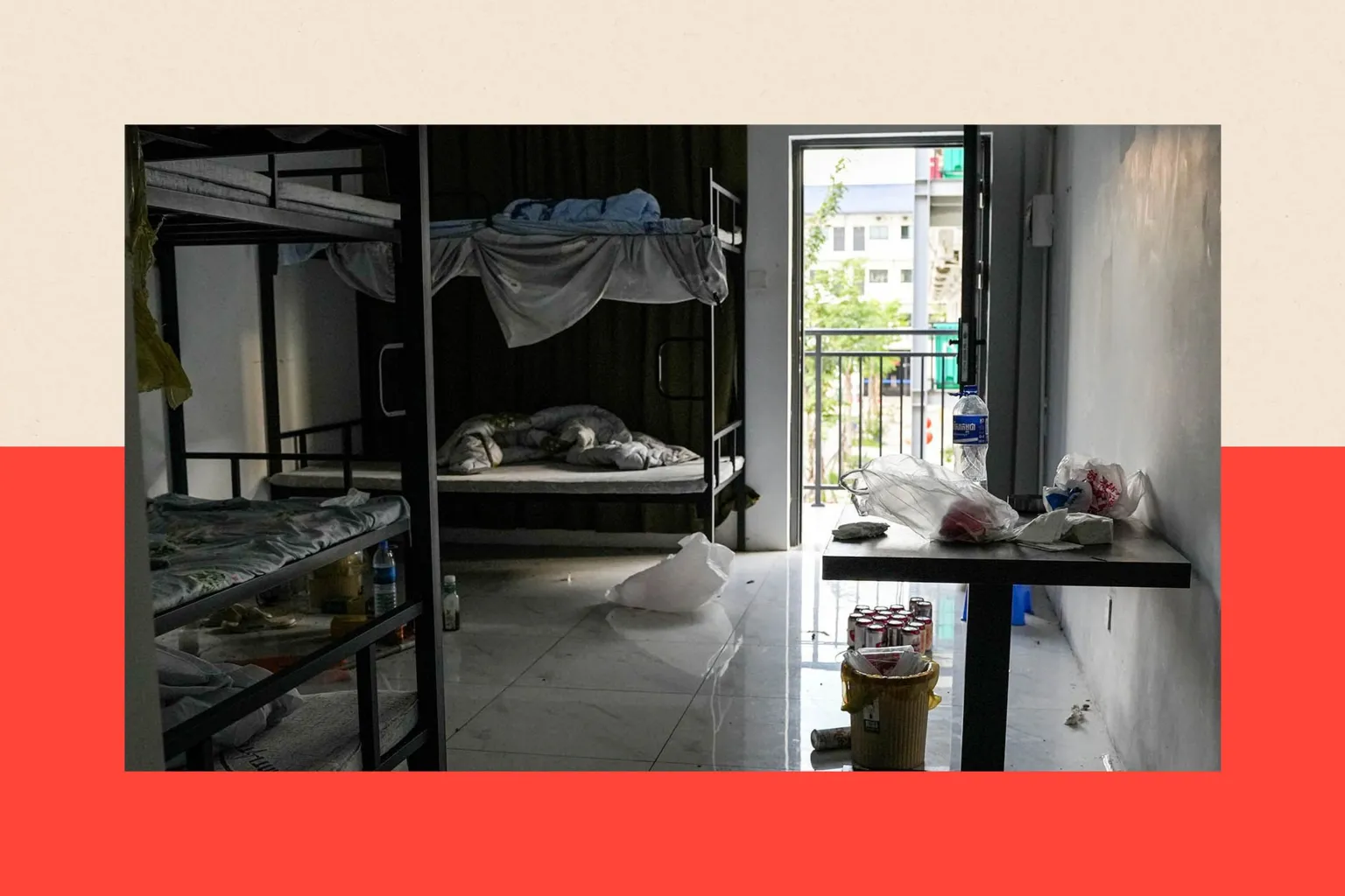  Leftover belongings lie scattered in a room inside a compound. Unmade bunkbeds, litter, and drink cans are in view. 