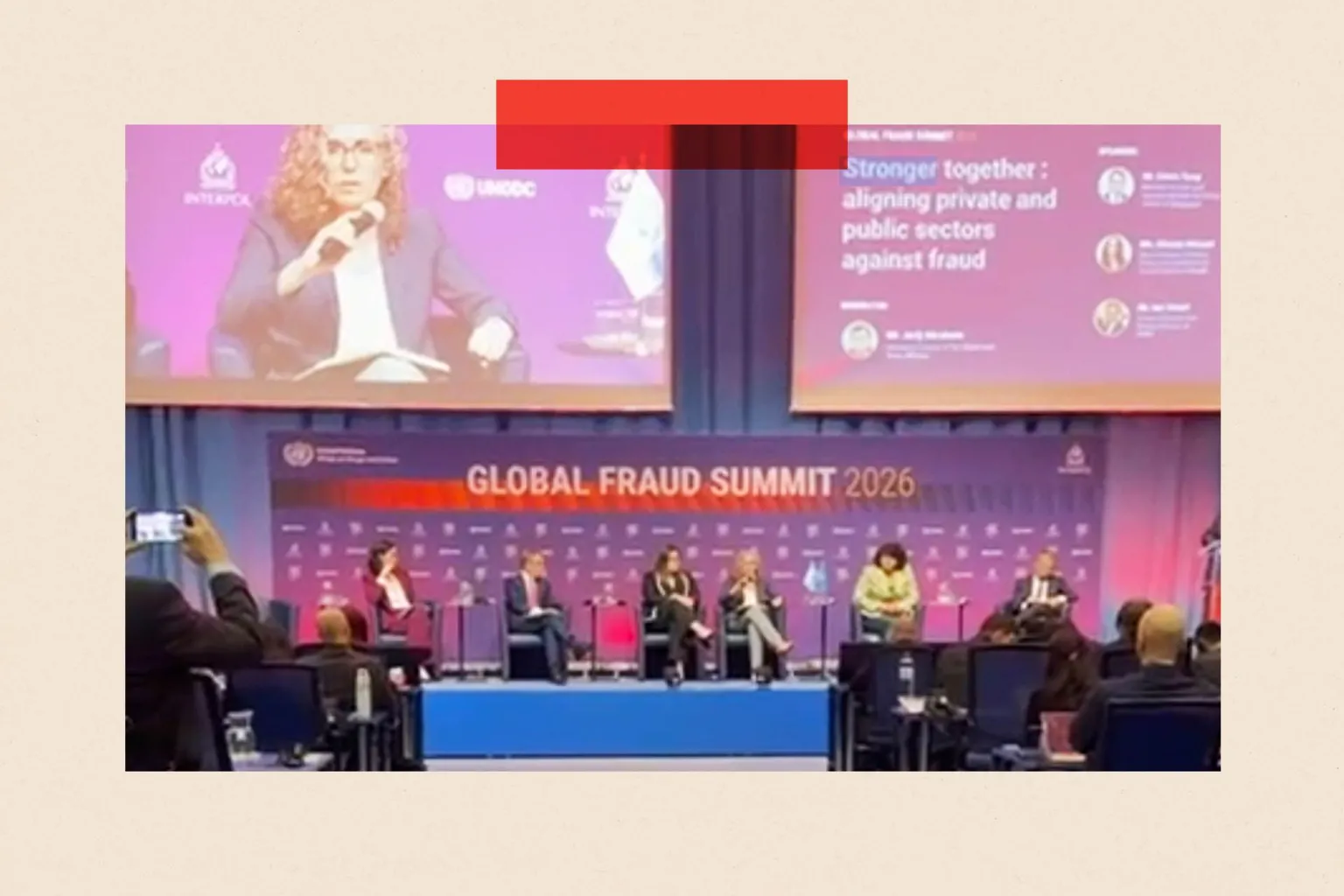 A stage with a purple backdrop and the words 'Global Fraud Summit' at the back, with six speakers sitting on the stage in front of an audience 