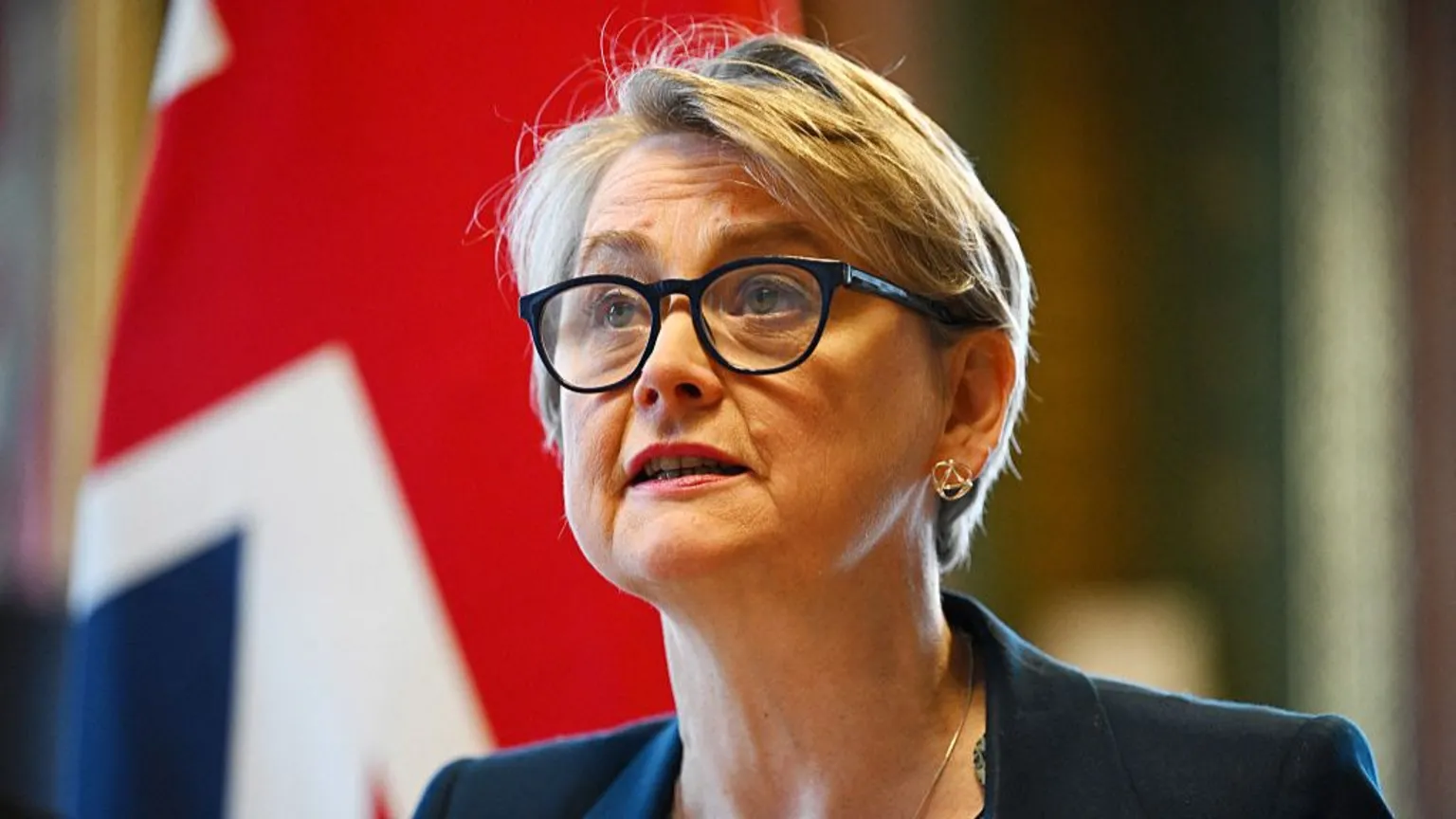 Leon Neal via UK Foreign Secretary Yvette Cooper wearing black rimmed glasses and a blue blazer, sitting in front of the British flag.