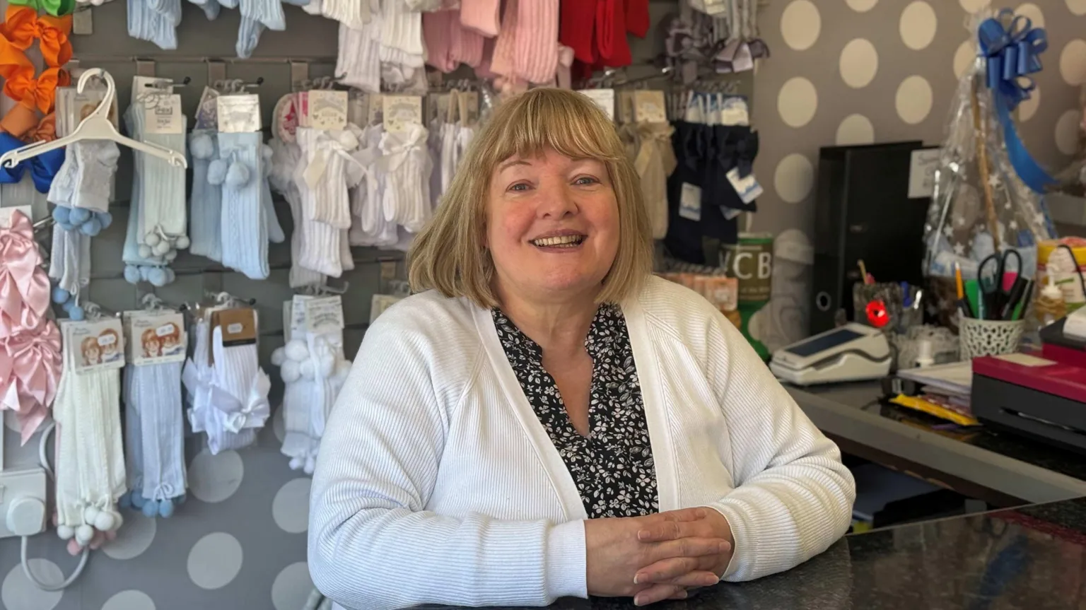 A woman smiles from behind shop counter 