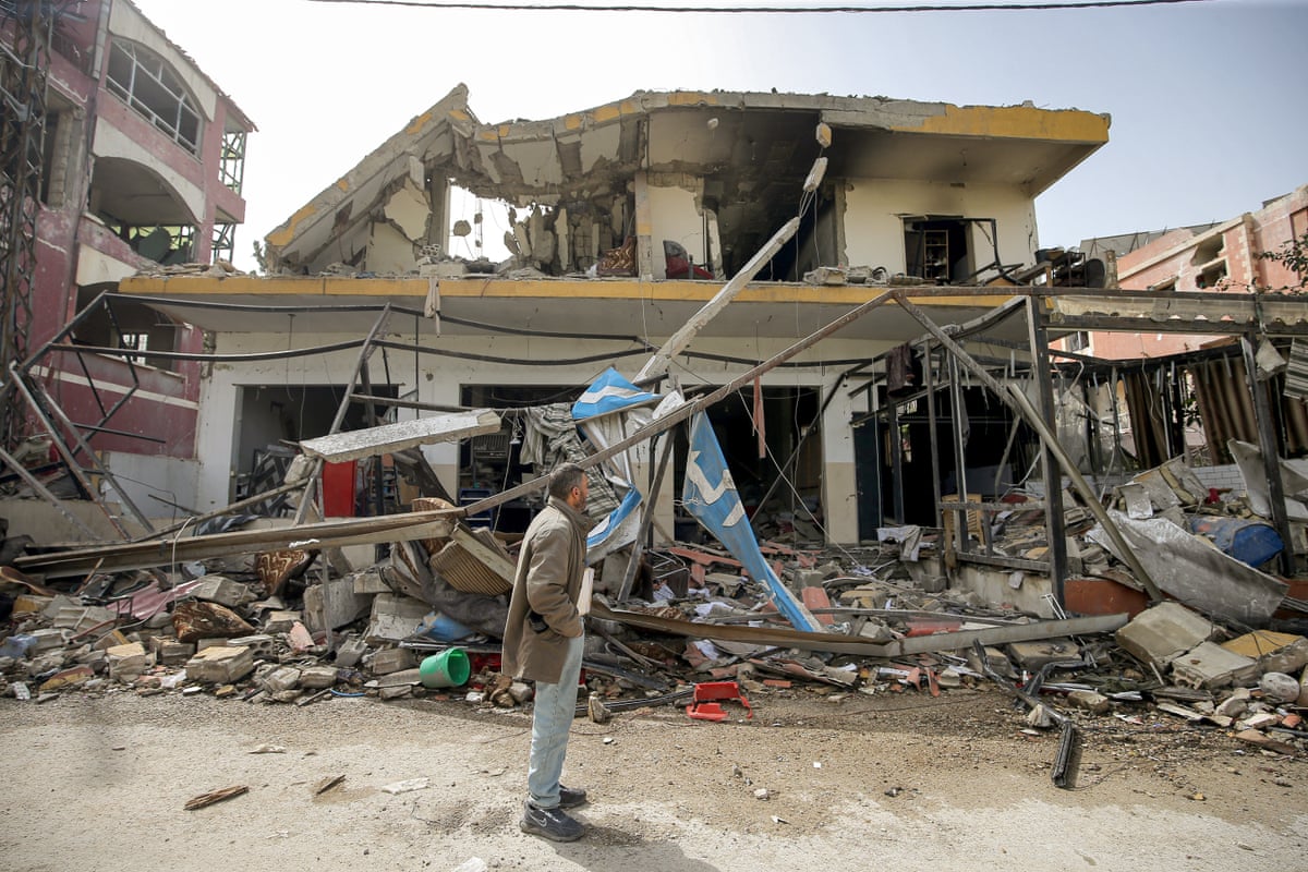 A man stands in front of a destroyed building. 