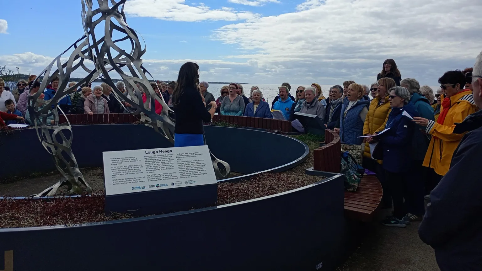 A choir singing standing outside. They are gathered around in a semi-circle.