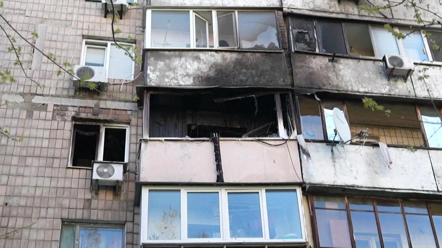  An exterior mid shot of an apartment block, showing the balcony of one apartment burned, as well as the exterior of apartments above it. 