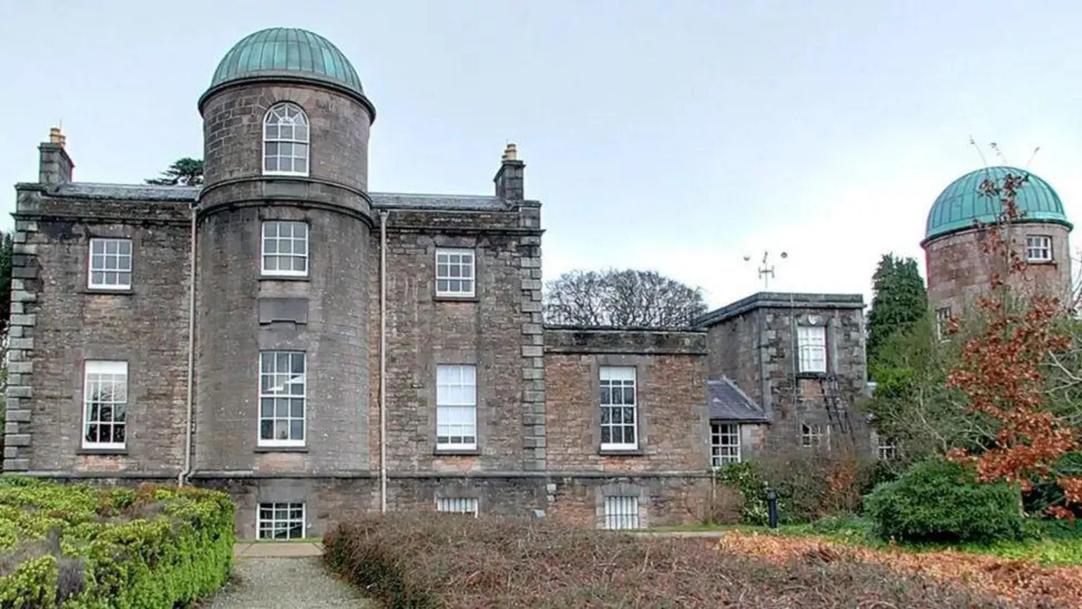 Armagh Observatory and Planetarium An exterior shot of a grey observatory building with blue copper domed roofs. The picture was taken during the day.