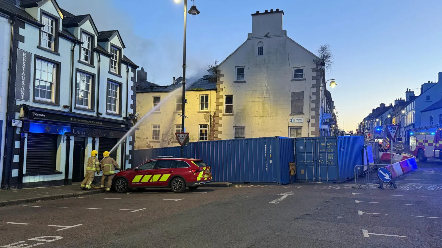 Two firefighters aiming water from a hose onto the roof of the building. 