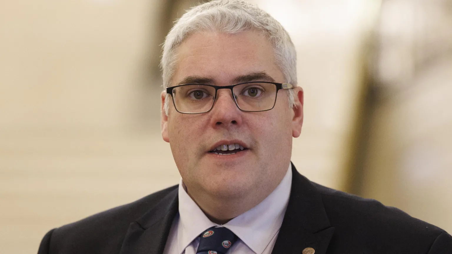 Liam McBurney/PA Wire Gavin Robinson wears glasses. He has a black suit on with a purple shirt and a tie. The background is blurred. 