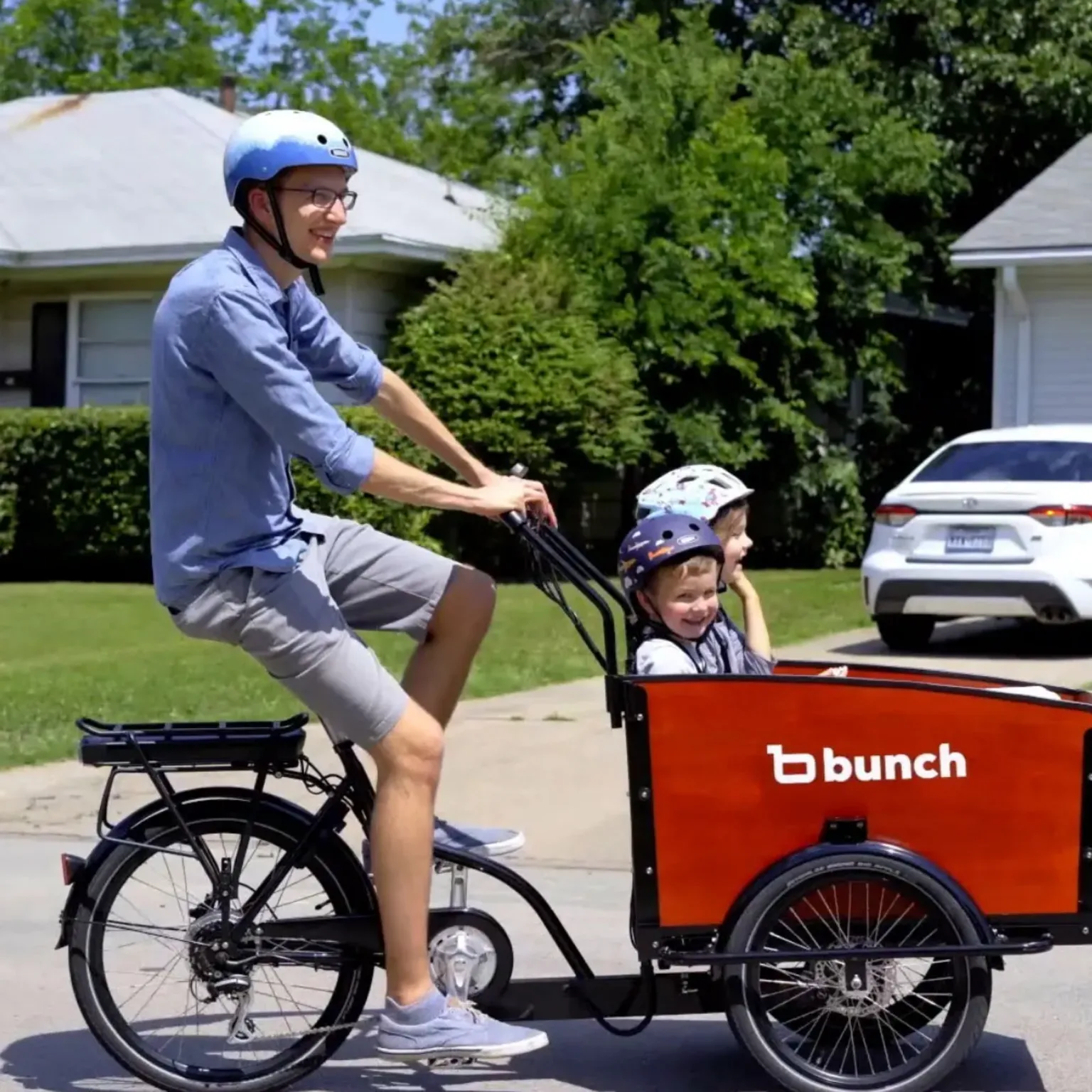 Bunch Bikes The founder and chief executive of Bunch Bikes, Aaron Powell, can be seen riding a black electric bike with a basket attached to the front in which his two children are sat. All three are wearing cycling helmets.