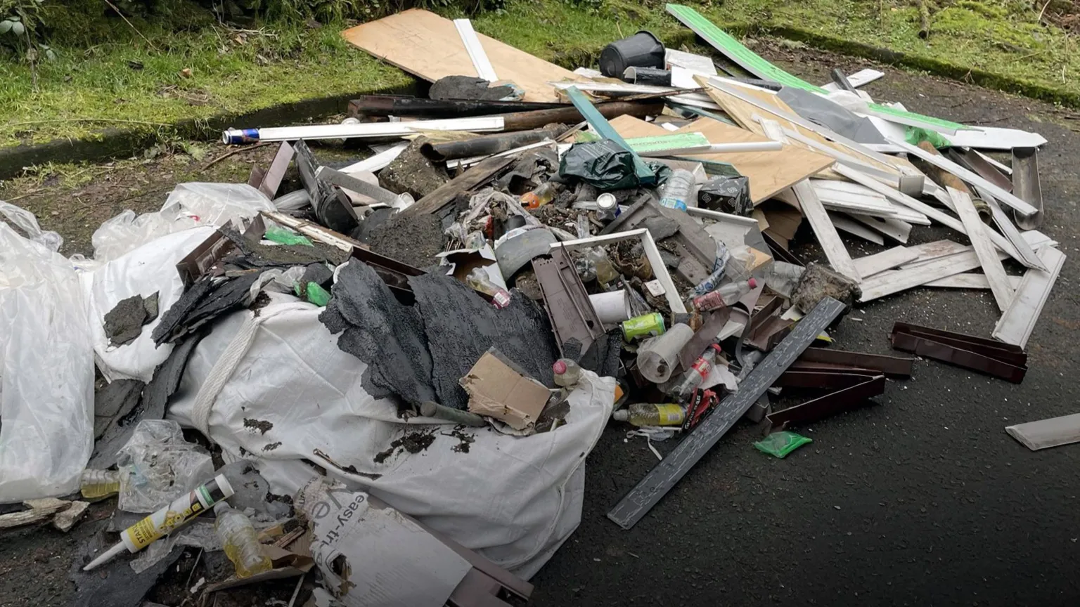 A close-up image of a huge pile of rubbish fly tipped in a layby near Luss - piles of strips of wood and mdf, empty cans and bottles, plastic, chunks of roof tar and general rubbish.