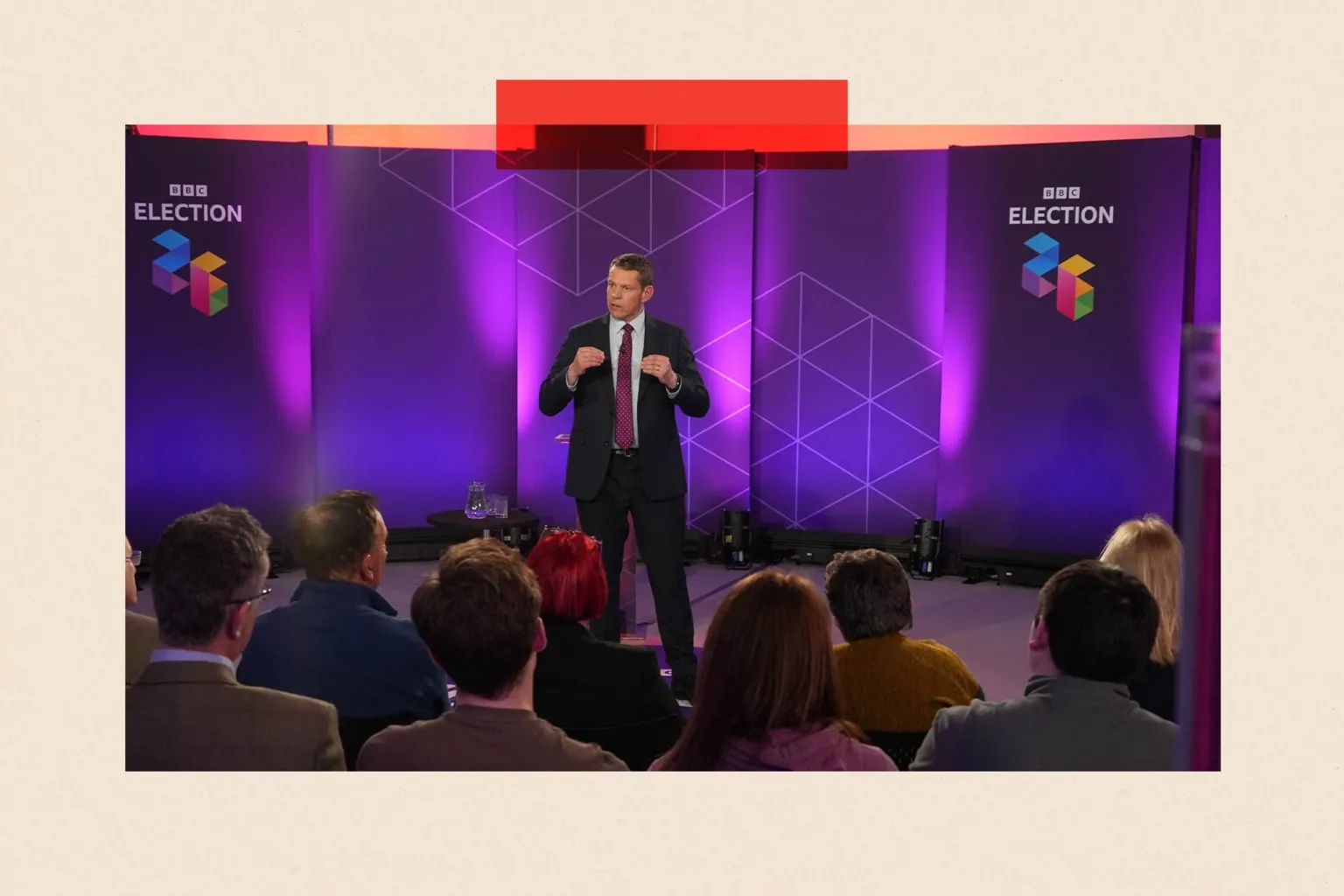 Plaid Cymru leader Rhun ap Iorwerth at a BBC Wales Ask the Leaders debate in Haverfordwest, Pembrokeshire. He is wearing a dark suit and a white shirt with a purple tie and stands in front of an audience, whose heads are visible from the rear. The words 