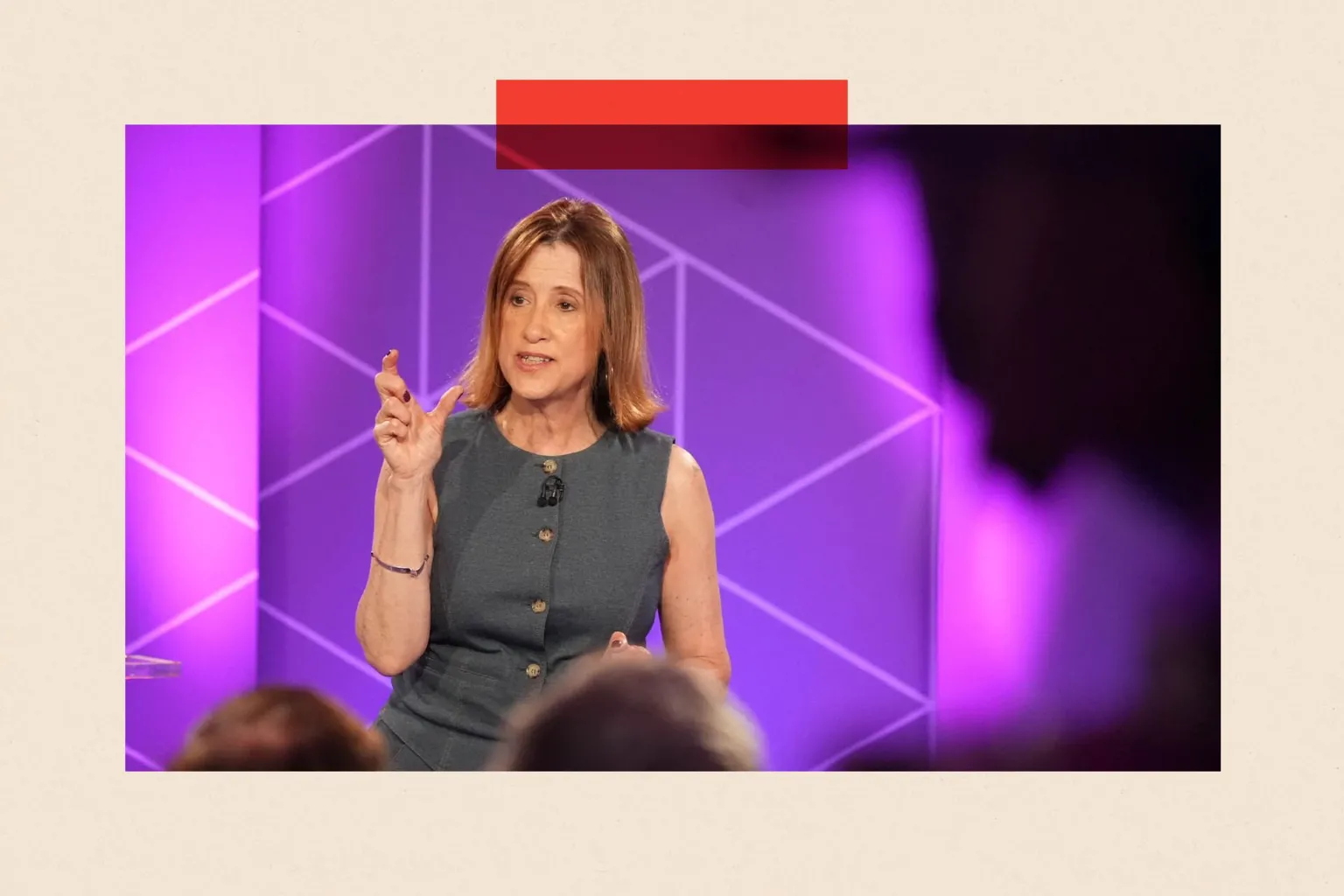 Jane Dodds, the leader of the Welsh Liberal Democrats, stands in front of a purple backdrop at the BBC leaders debate. She wears a grey sleeveless top and is gesturing with her right hand.