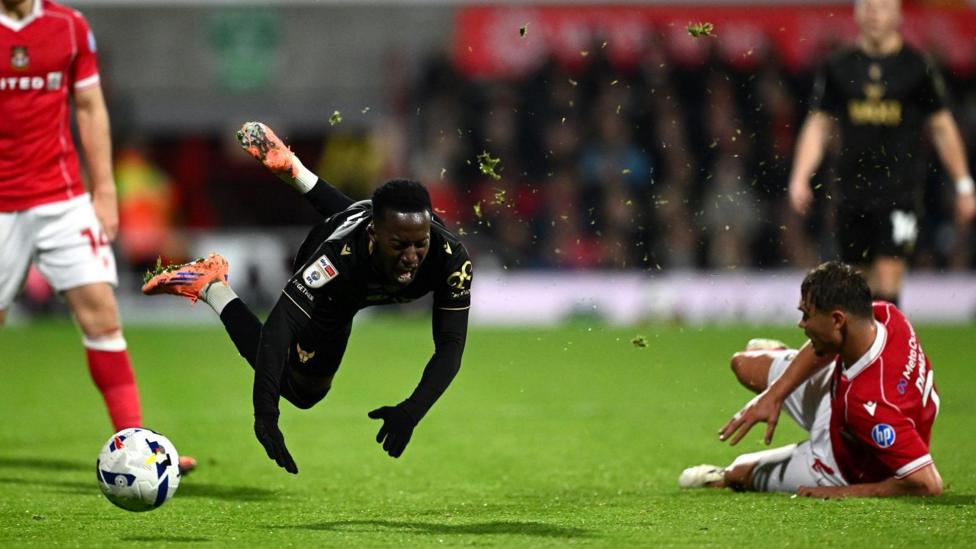 Oxford United's Siriki Dembele is in the air with Callum Doyle sliding across the pitch after a tackle 
