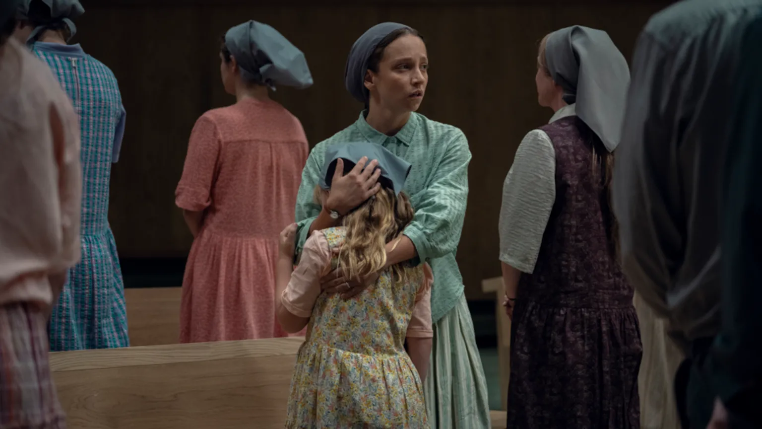 Netflix A woman in a long dress and head covering hugs a child. She looks concerned. There are other women around her.