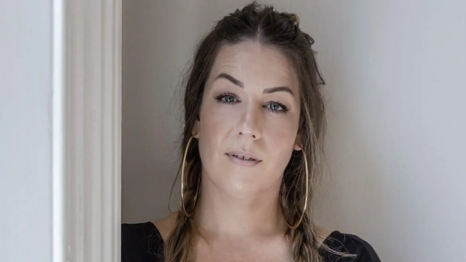 Mia Doring A woman with brown hair and large gold hoop earrings looking at the camera.