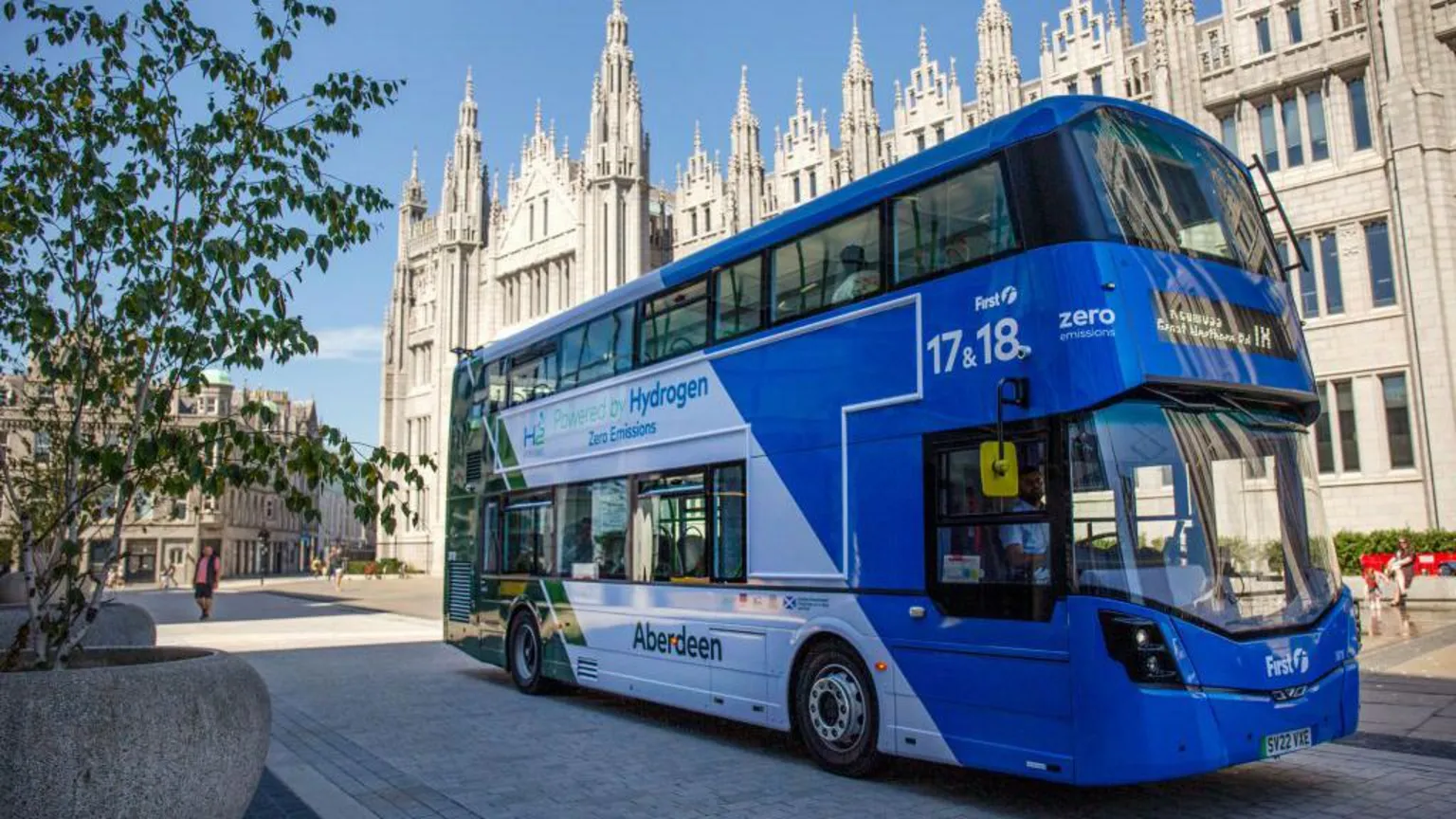  A hydrogen bus with bright blue, white and green colours if front of a building with many spires in the heart of Aberdeen