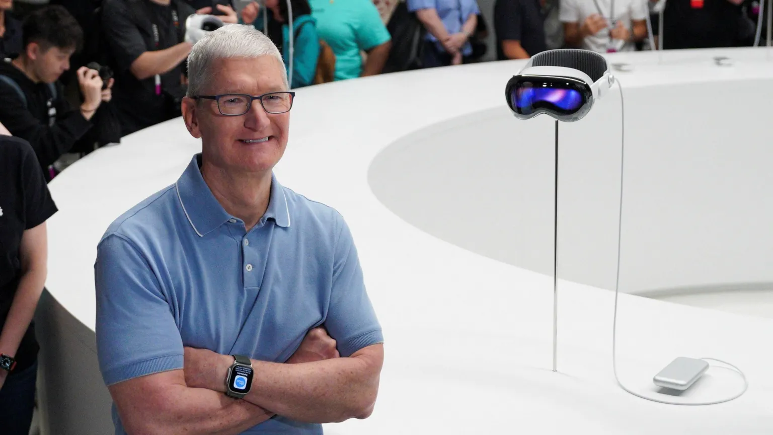 Tim Cook wearing a light blue polo shirt, standing next to the Apple Vision Pro headset.