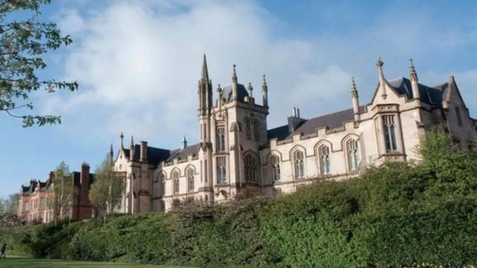 UU The university campus in Londonderry. A number of bushes and grassy areas can be seen in front of a Gothic-looking building with several large windows.