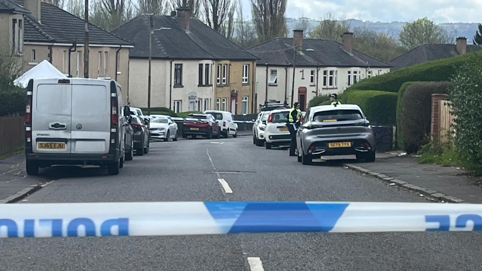 Blue and white police team in the foreground of a street scene. cars are parked on both sides of the road and two police officers can be seen in the distance.