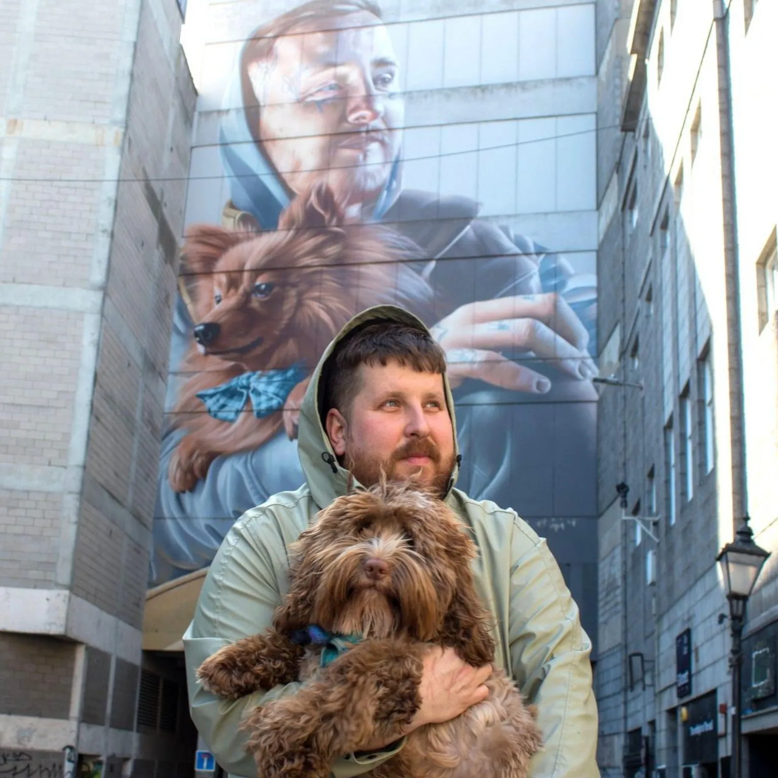 Nuart 2026 A man holding a dog, recreating a large mural on a wall in the background.