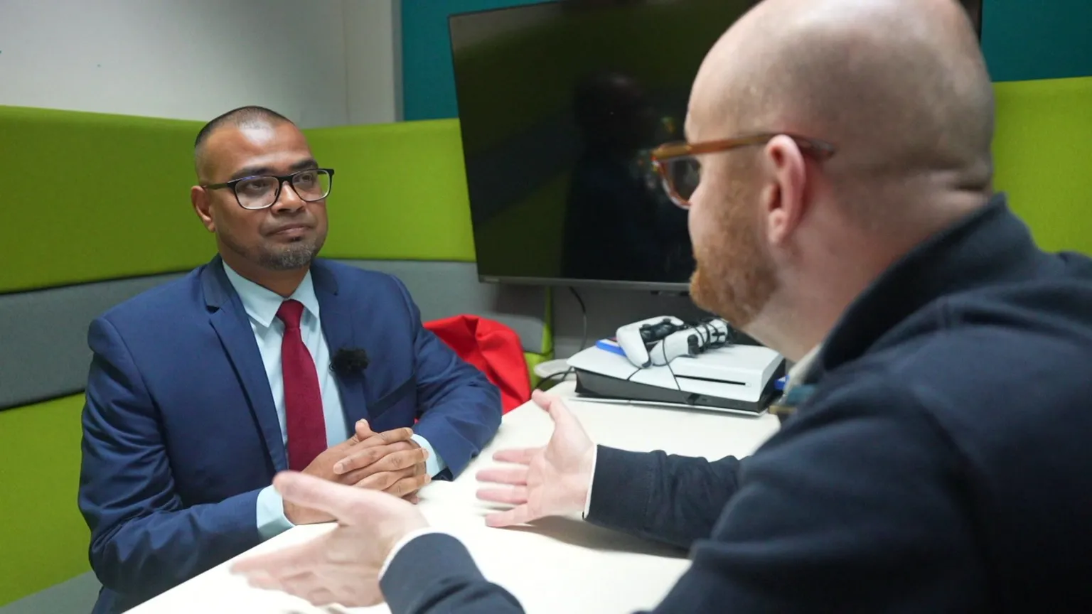 A man in a navy suit and red tie, Mahaboob Basha, speaks to a man in a blue jumper, reporter David Grund