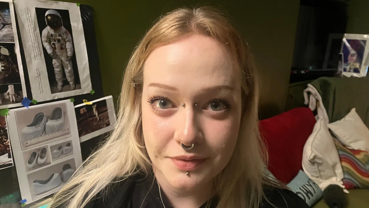 A woman, pictured from the shoulders up, with long blonde hair. She has a number of piercings on her face. 