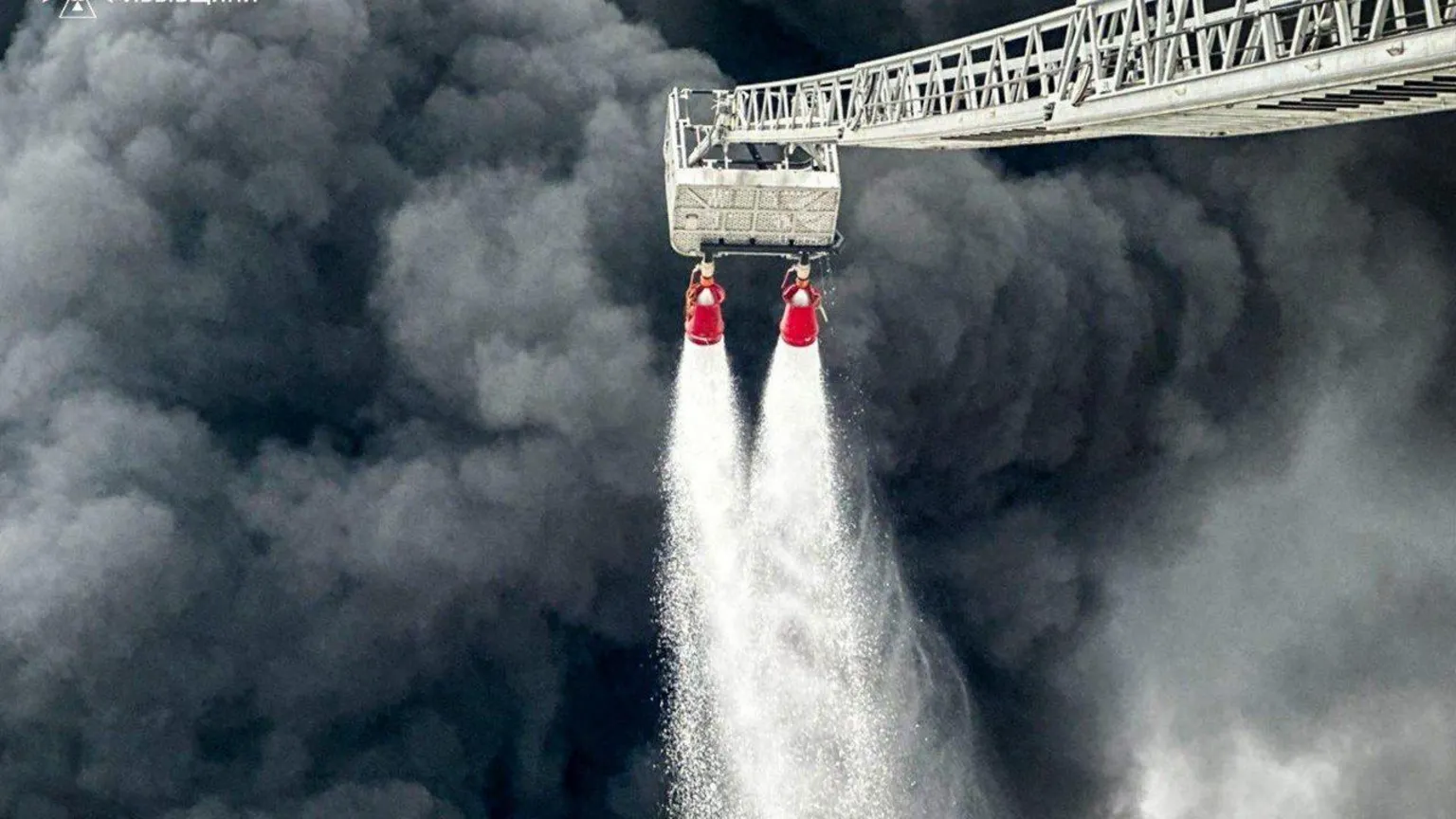 DSNS Thick dark grey smoke billows from the Brody oil hub as firefighters tackle an unseen fire with two hoses from an extended ladder.