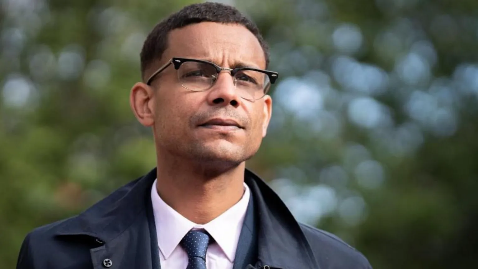  Daniel Kebede, a man in a pink shirt and blue tie with a dark blue coat and glasses. 