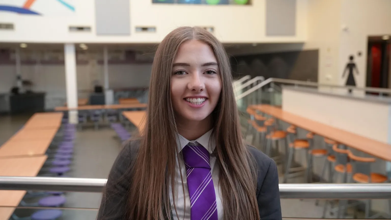 Hannah Karpel/BBC A teenager with long straight dark hair smiles at the camera. She is wearing a dark school blazer and a purple tie. 