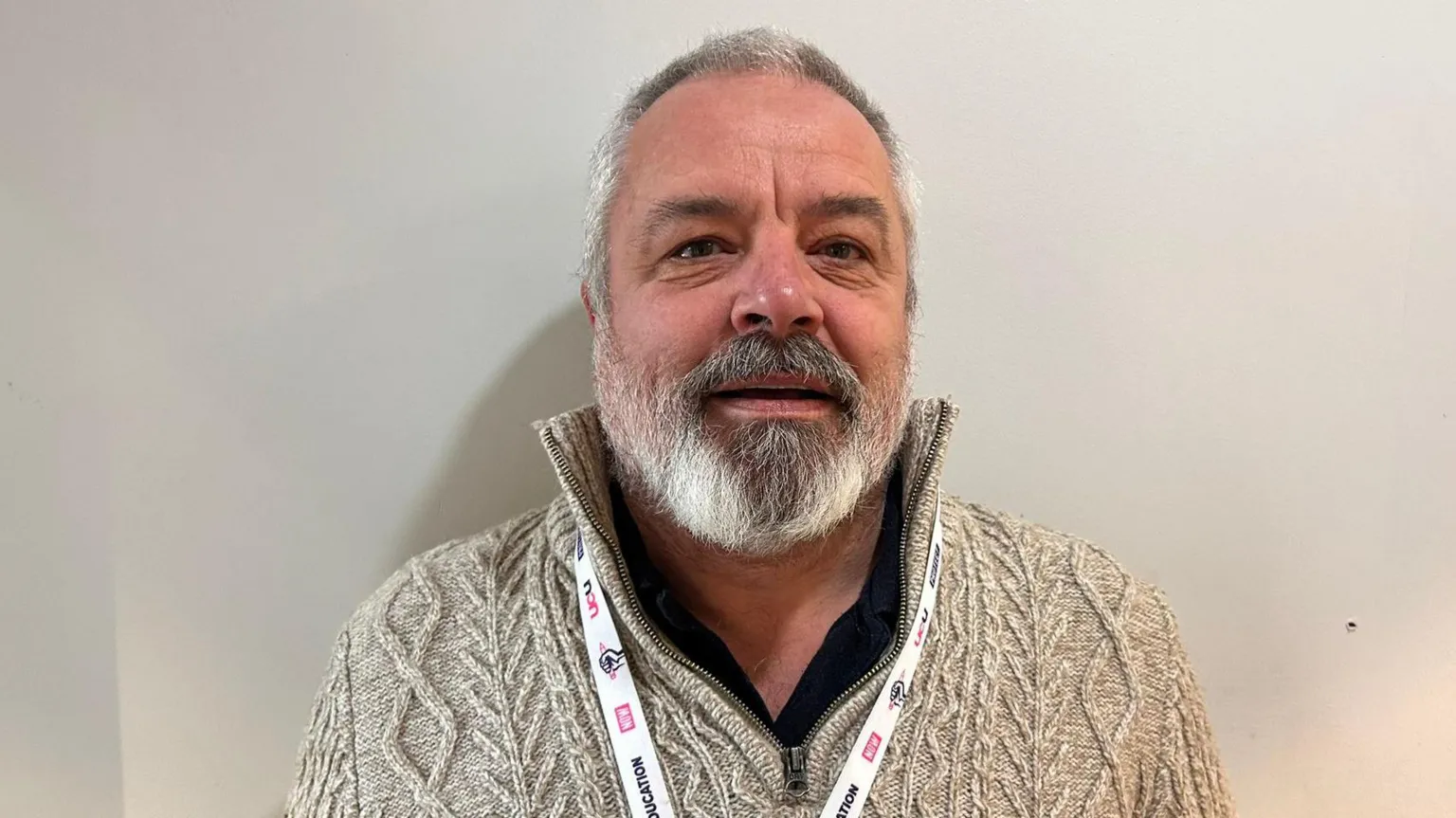 Norman Hagan has short hair and a beard. He is wearing a wooly white fleece. 