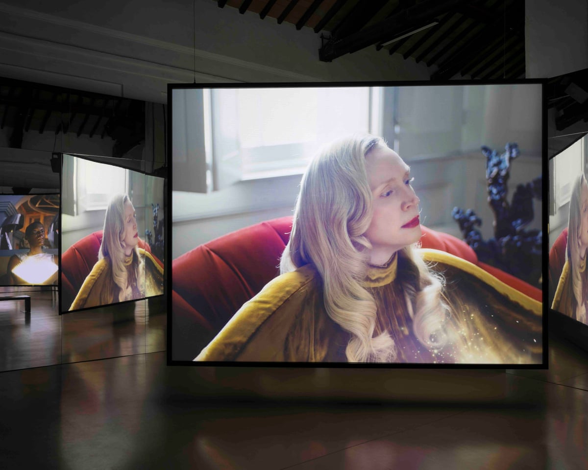 An installation featuring two screens of a film by Issac Julien starring Gwendoline Christie (pictured) sitting in a red chair wearing her long blond hair down.
