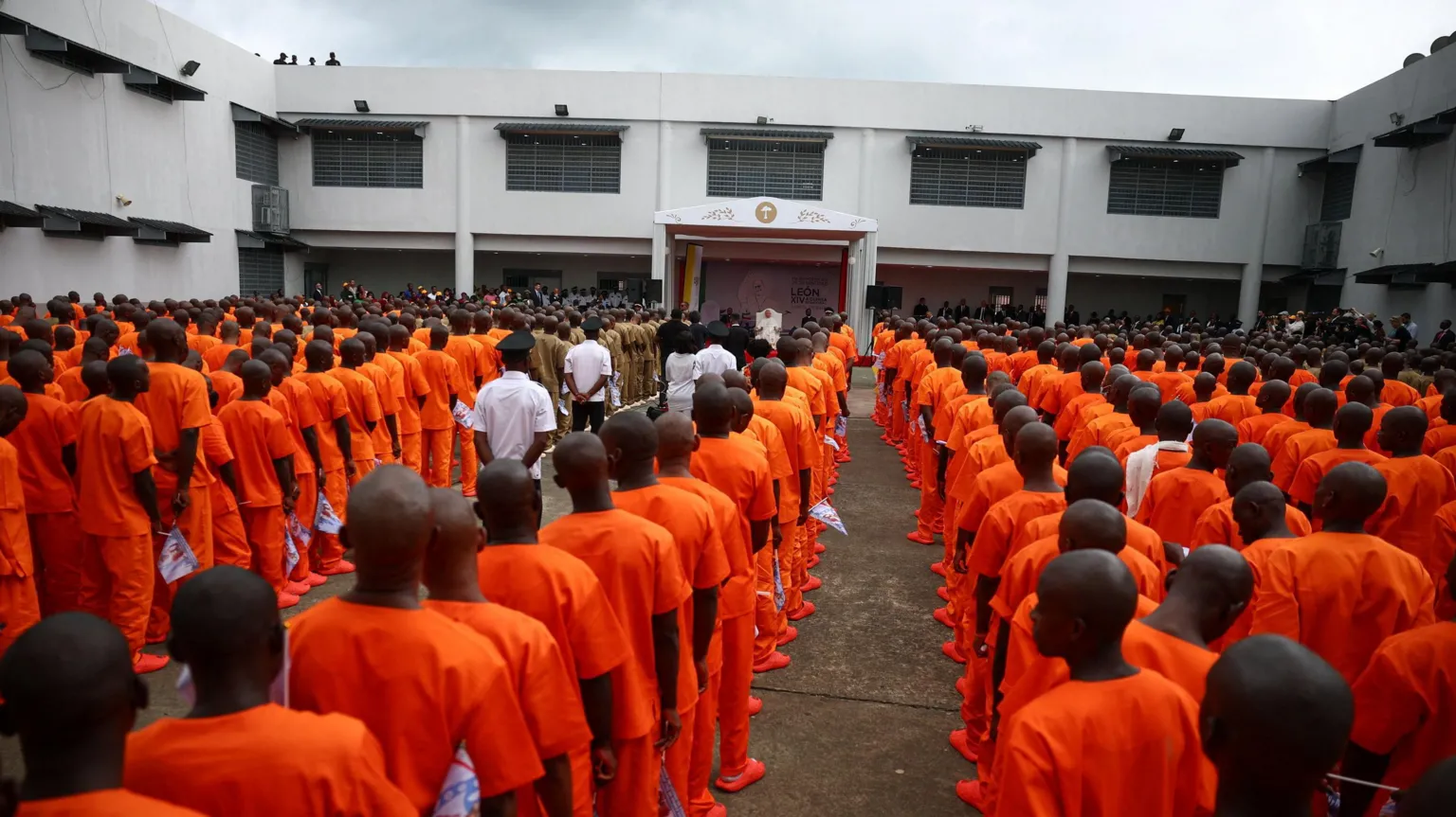  Dozens of prisoners in orange uniforms line up in front of the Pope, who can be seen in the distance under a shelter