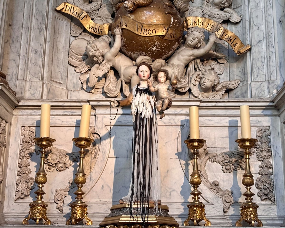 A wooden statue of the Virgin Mary dressed in a white dress trimmed with pigeon feathers.