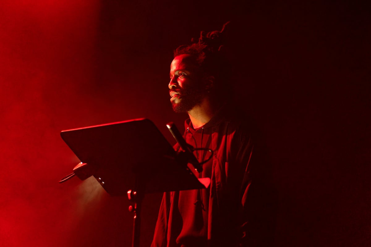 Simeon Barclay dimly lit in red light, performing spoken word.