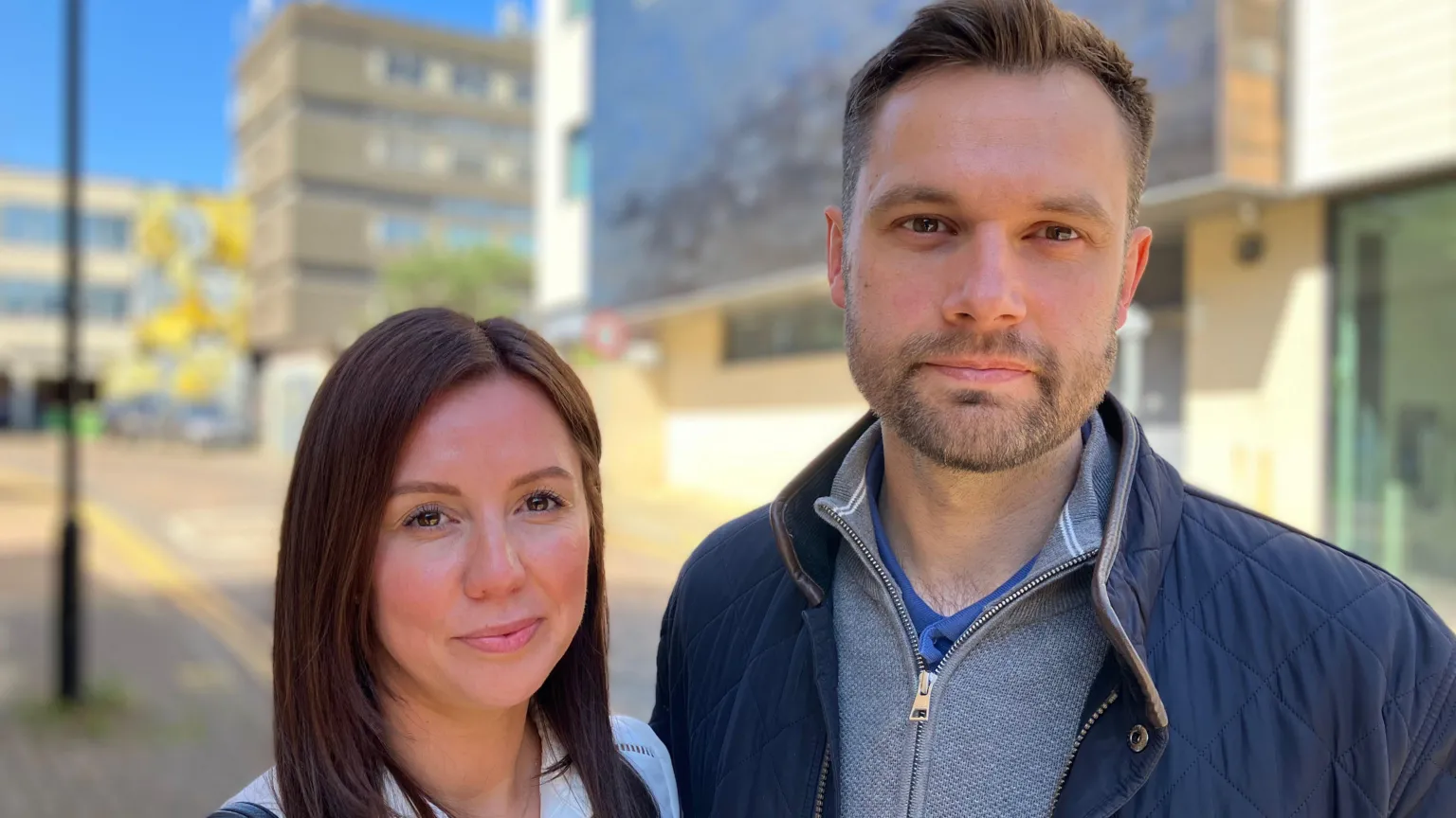 Lewis Adams/BBC Lucy Davies, who has long brown hair and is wearing a white shirt, standing next to Rob Davies. He has short brown hair and is wearing a navy jacket over a grey jumper.
