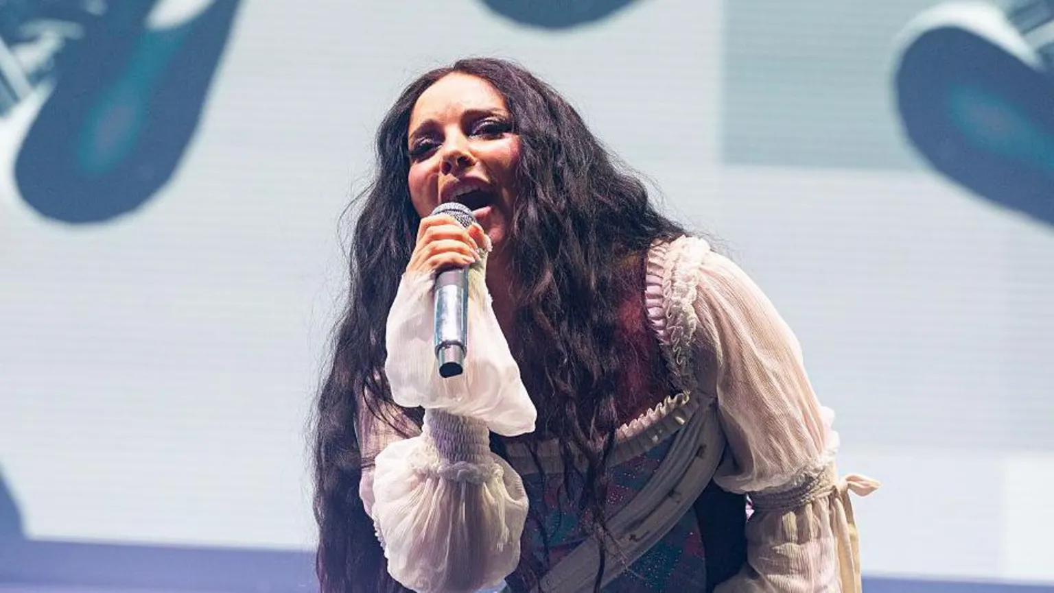  Music artist Jade, singing into a microphone, while wearing a white sleeved outfit,