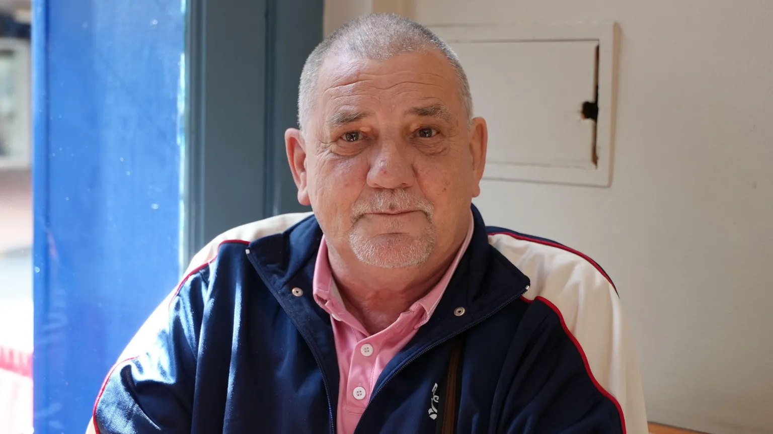 Steven Rees-Davies has very short grey hair. He is wearing a pink polo shirt and a navy and white jacket. 