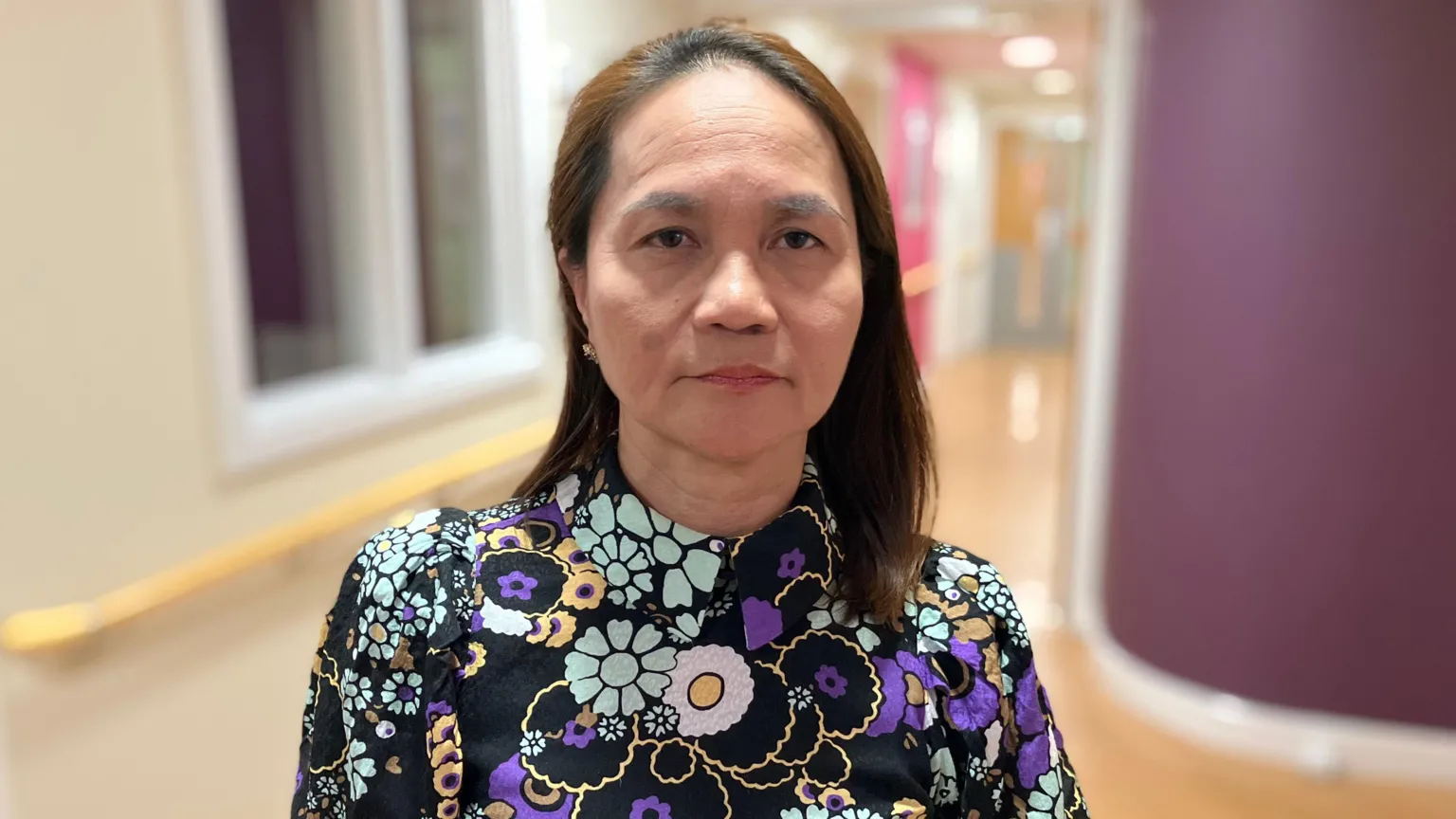 Arlene Elano has medium length brown hair. She is wearing a black blouse with purple, pink and light blue flowers.