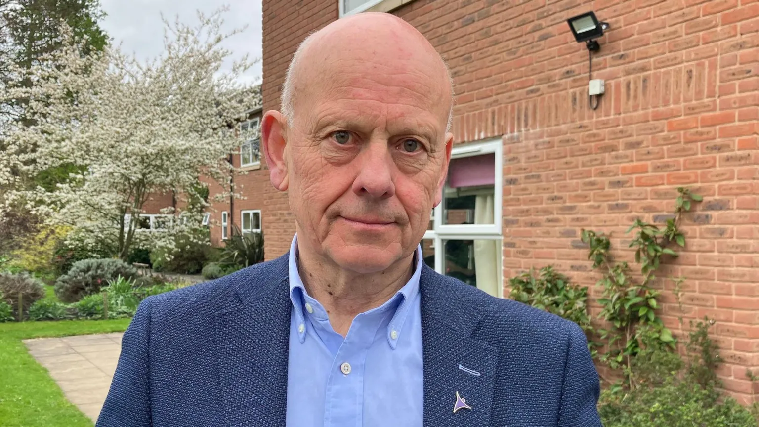 Mario Kreft has short white hair on the sides of his head. He is wearing a blue shirt and navy blue jacket. He is stood outside Bodlondeb care home in Wrexham.