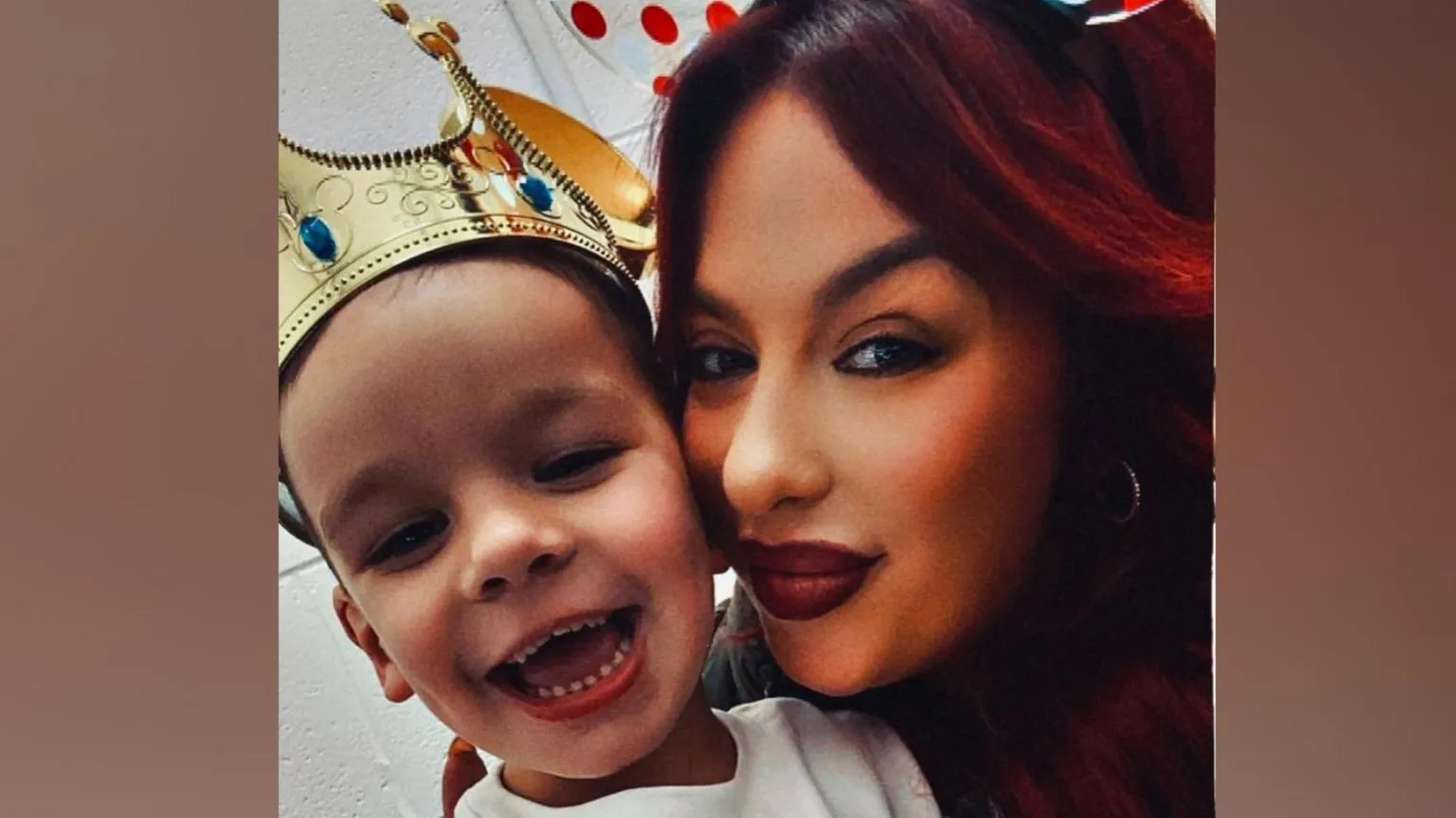 Kendra Hazlett A young smiling boy wearing a gold crown is hugged by a smiling lady with red hair 