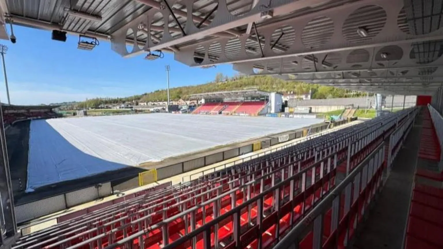 A number of seats are visible at the Ryan McBride Brandywell Stadium. A large white tarpaulin sheet is covering the football pitch. 
