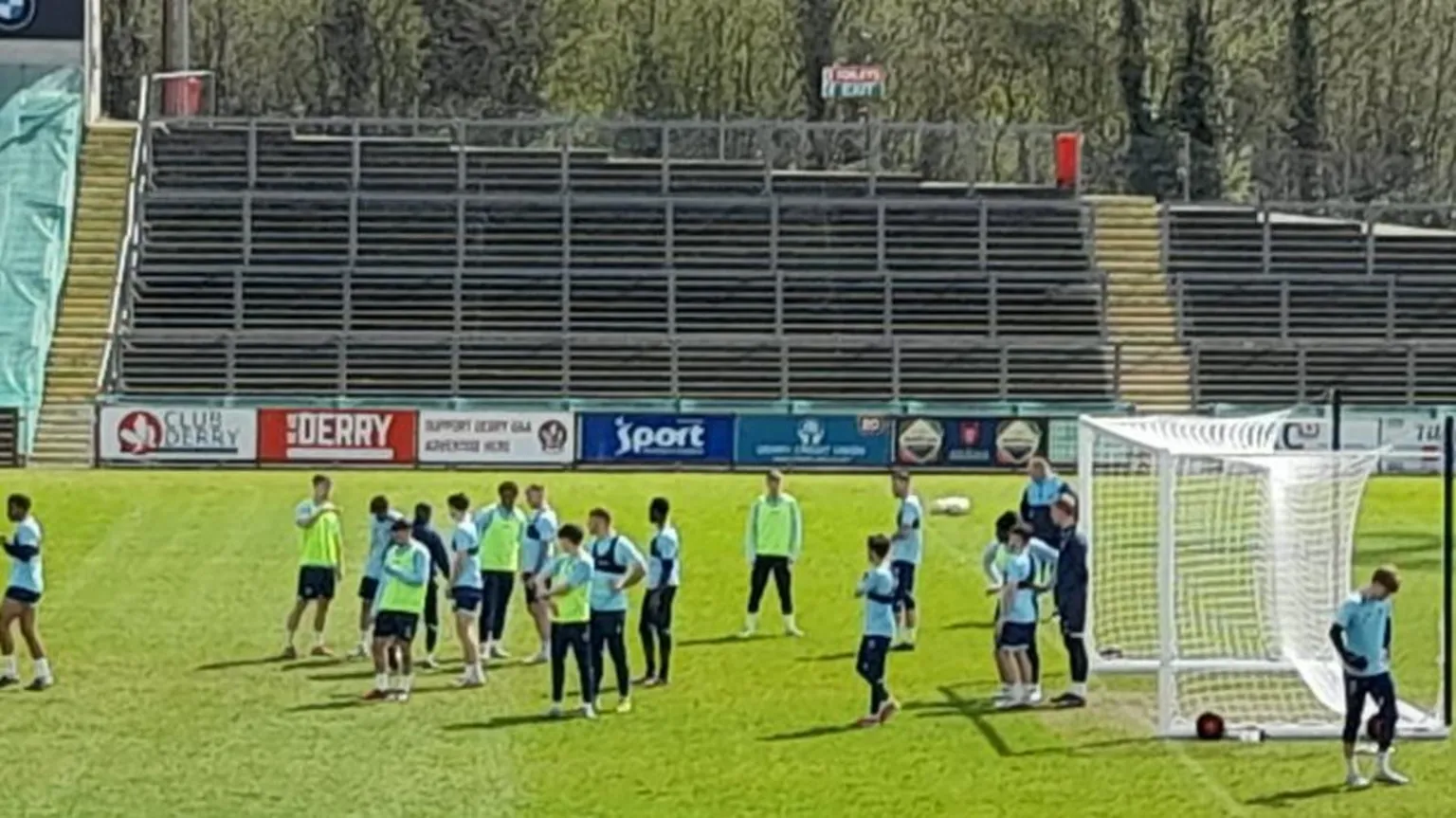 Shows 19 male footballers in a training session at a stadium