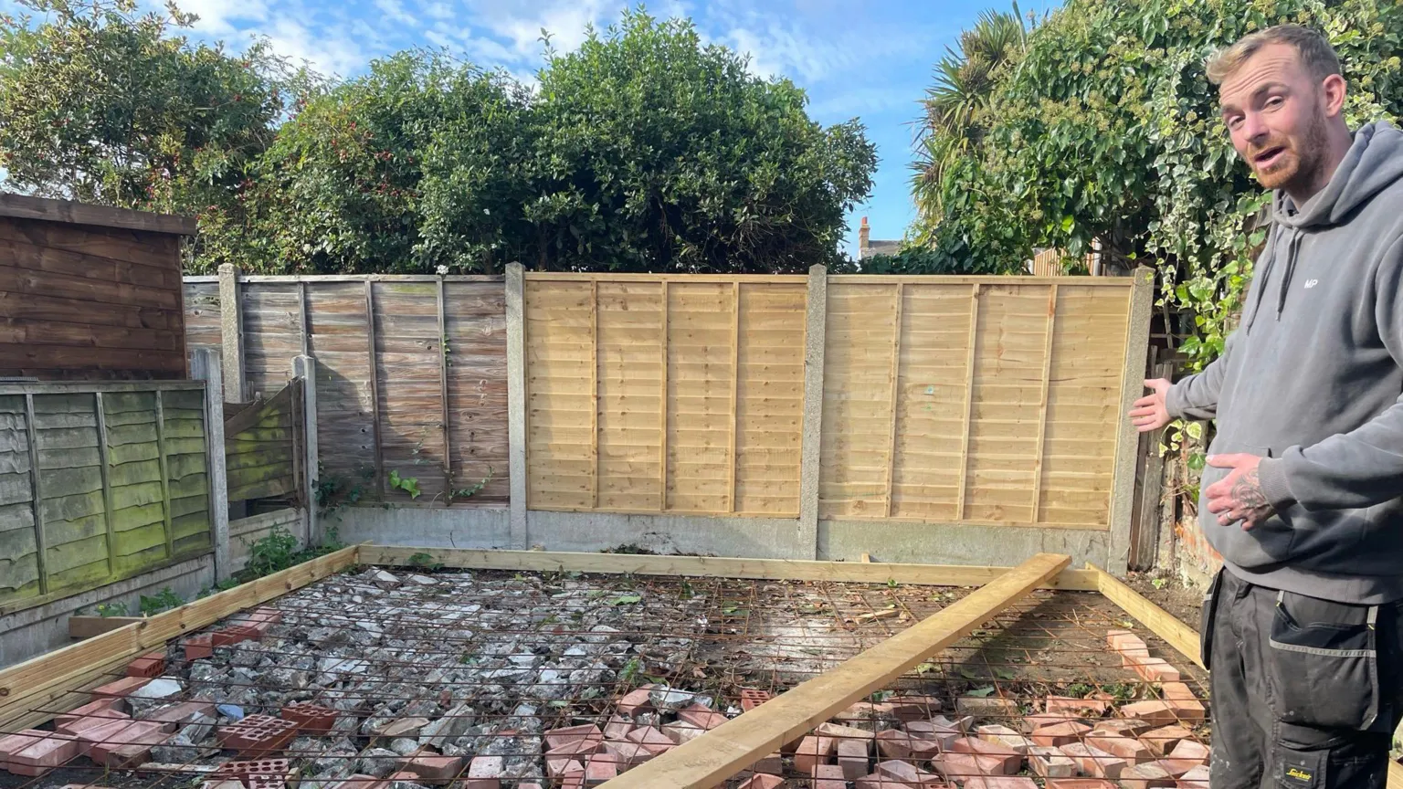 Gemma Hemmings Steve Figg, who is wearing a grey hoodie and trousers, pointing at the foundations of what was to become the garden office.