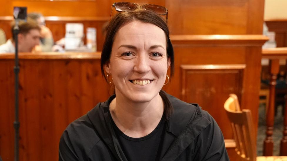 Natalie Wasiuk. Mae'n gwisgo siaced ddu a sbectol haul ar ei phen.