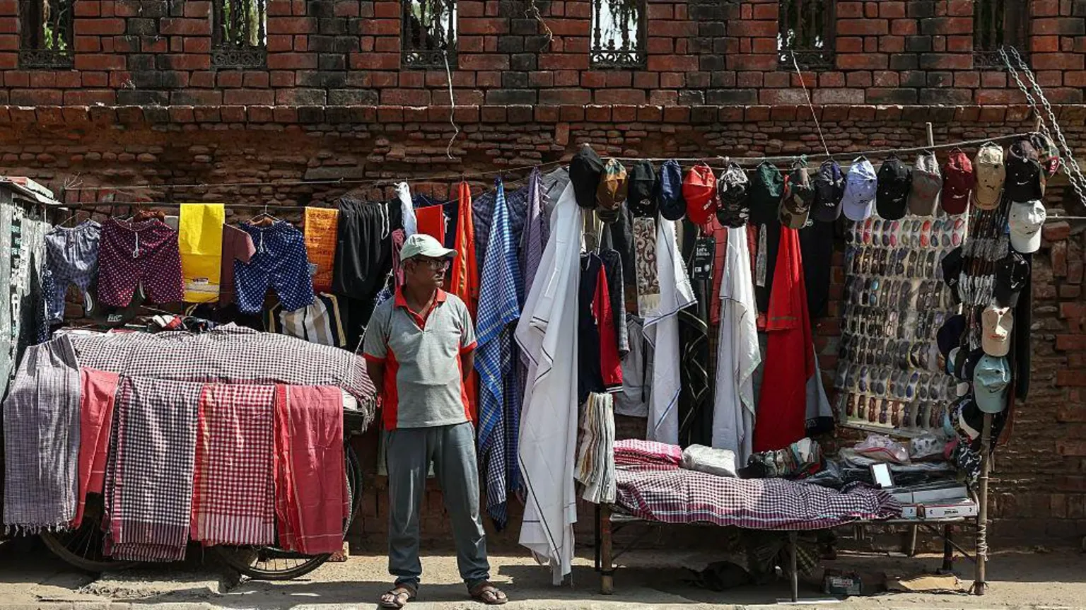  A vendor selling clothes, caps and other accessories waits for customers at his roadside stall on a hot summer day in Varanasi on April 18, 2026.