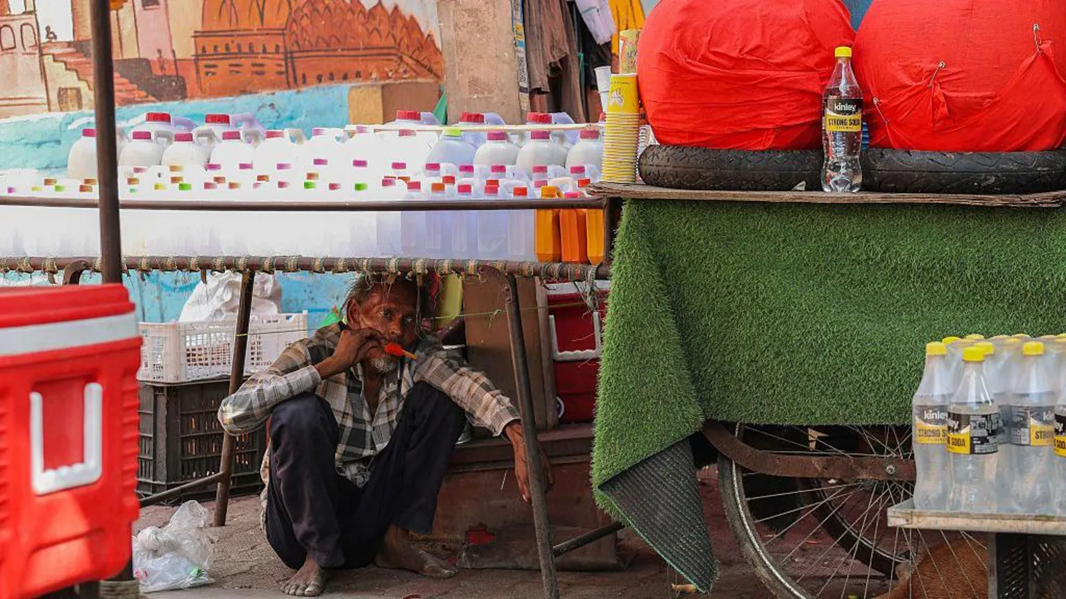  A man eats ice-cream while taking shelter under a roadside stall on a hot summer day in Varanasi on April 23, 2026