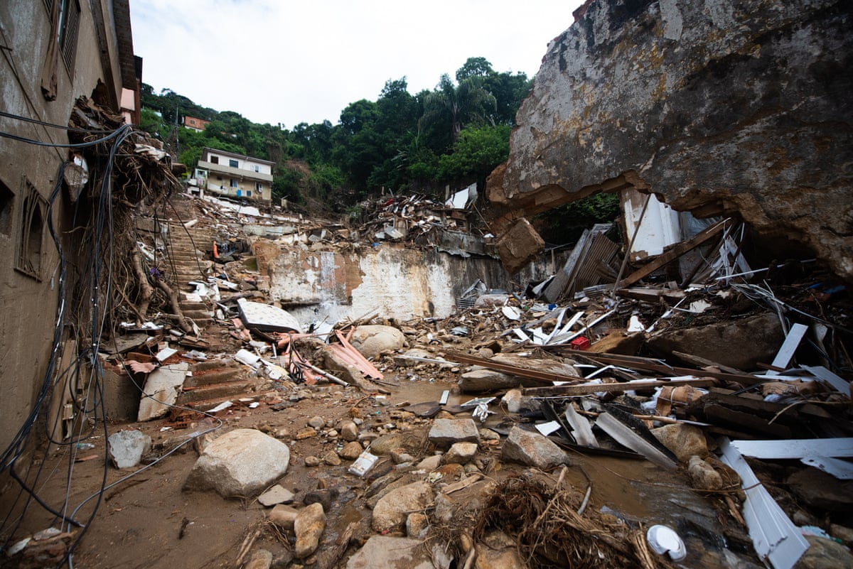 The aftermath of the devastating mudslide, showing mud and debris on a steep hillside between destroyed buildings.