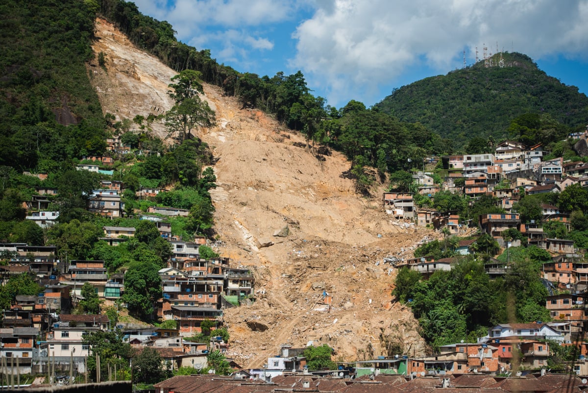 A wide swathe of mud cuts between houses on a steep hillside. Fragments of buildings can be seen among the dirt.